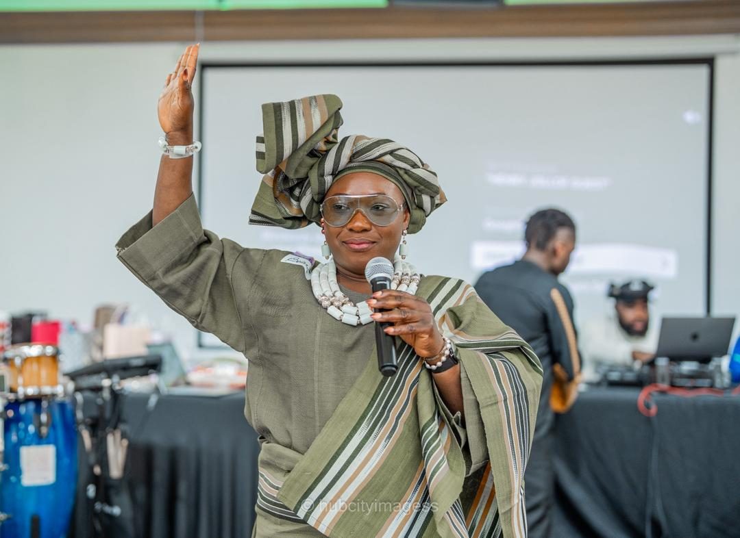 Host in green aso-oke and gele addressing the room with a mic