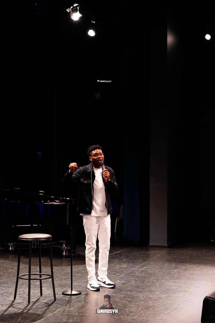 Comedian on a spotlit theatre stage with a mic stand
