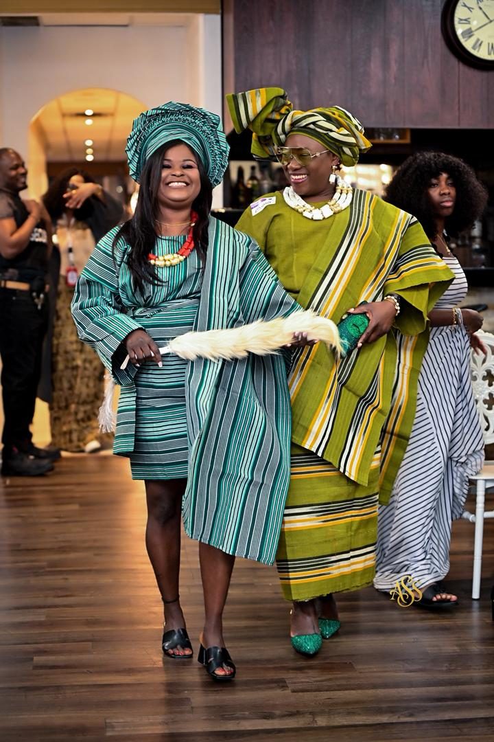 Two guests in green and teal traditional aso-oke attire walking through a venue